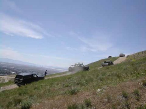 1994 Ford Bronco - Several off-road vehicles ascend a dusty incline on a sunny day, with a town visible in the valley below.