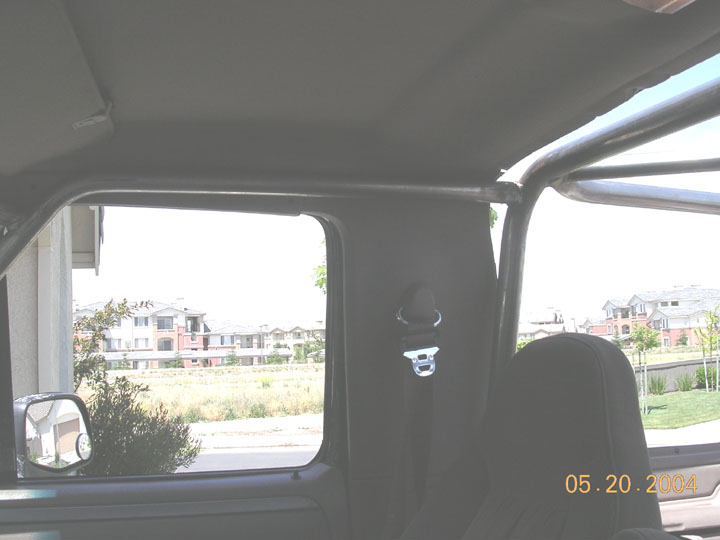 Bronco interior with gray roll cage, headliner, seatbelt and seat, field and homes outside window