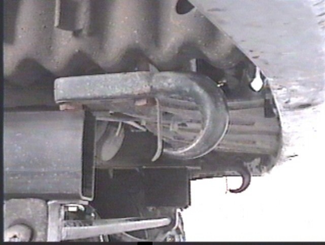 Underside close-up of a trailer hitch crossmember and curved bracket below tire tread