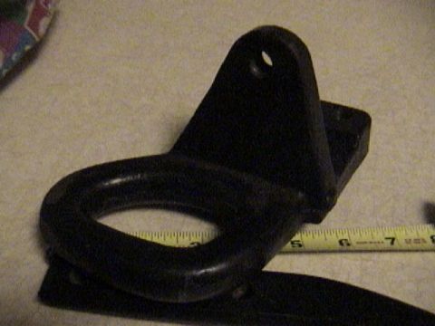 1995 Ford Bronco - A black metal tow hook or lifting bracket with a rounded loop and a mounting plate featuring a bolt hole tab, resting on a light-colored su…