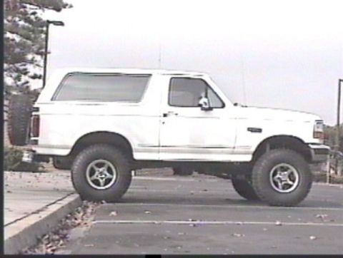 1993 Ford Bronco - Side view of a white 1993 Ford Bronco, parked on a curb with a spare tire on the back.