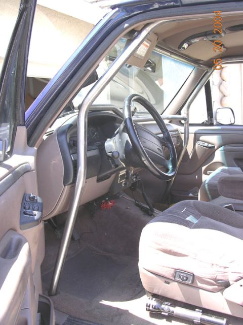 1994 Ford Bronco - The interior of a truck features a roll cage, seats, and dashboard with a flashlight on the floor.