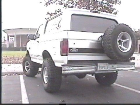 1993 Ford Bronco - Rear view of a white Ford Bronco with a spare tire mounted externally and lifted suspension.