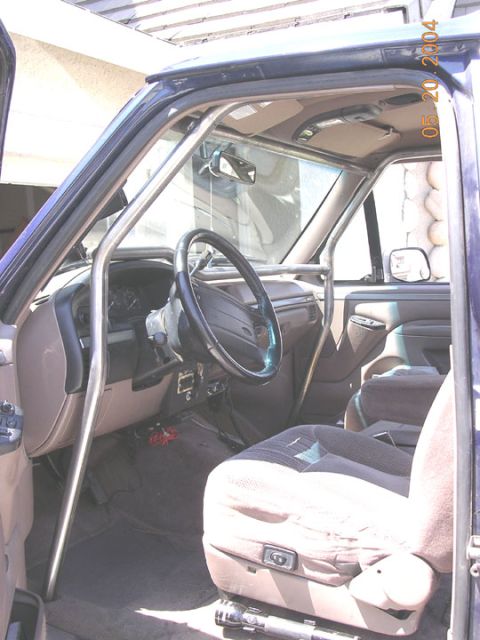 1994 Ford Bronco - The interior of a modified SUV shows a custom roll cage installed around the driver and passenger seats.