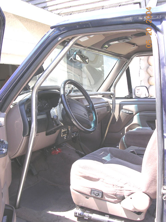 Ford Bronco interior with roll cage bar, tan dash and black cloth seats, door open