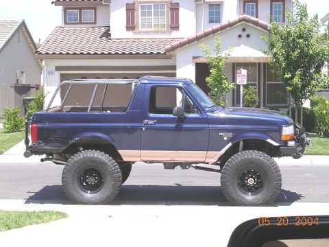 1994 Ford Bronco - A blue 1994 Ford Bronco with tan lower body trim and aftermarket wheels is parked on a suburban street.