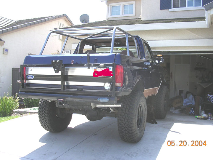 Rear of dark blue Ford Bronco with roll cage, big tires, parked in driveway