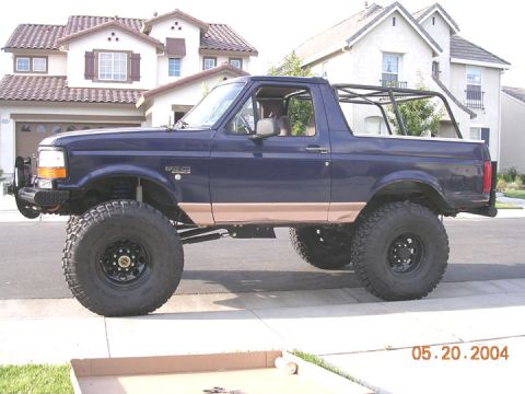 1994 Ford Bronco - This lifted blue Ford Bronco with tan trim and a roll cage is parked on a suburban street.