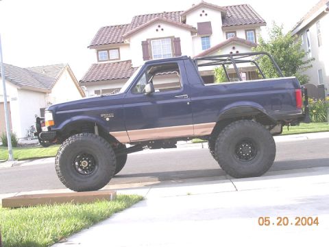1994 Ford Bronco - This lifted 1994 Ford Bronco features a prominent roll cage and tan body trim, seen here in a side profile.