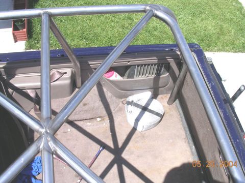 1994 Ford Bronco - A roll cage is installed in the bed of a blue pickup truck, with a seatbelt and storage compartment visible.
