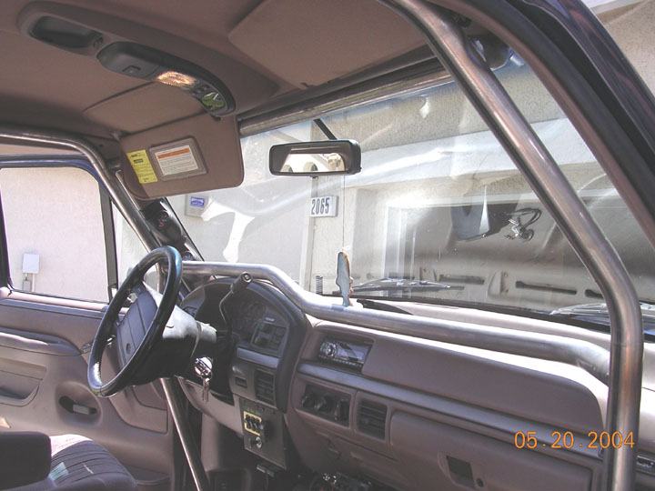 Truck interior with tan dash, black steering wheel, rearview mirror and metal roll cage bar by windshield.