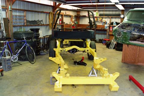 1990 Ford Bronco - A vehicle chassis is elevated on jack stands in a workshop, with another vehicle partially visible to the right.