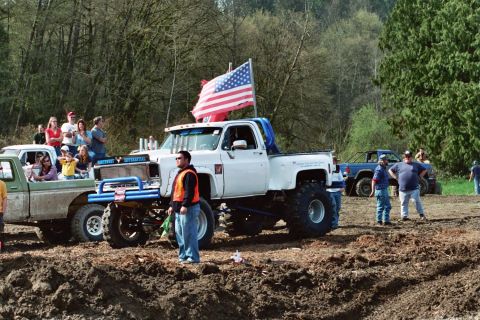 1990 Ford Bronco - Several lifted trucks are gathered in a muddy outdoor area, with spectators watching the event.