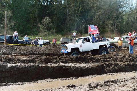 1990 Ford Bronco - Several trucks and spectators gather for a mud bogging event, with one white pickup truck stuck in the mire.