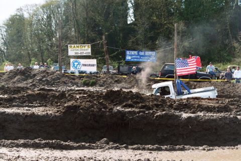 1990 Ford Bronco - Trucks compete in a mud bog event, with one vehicle deeply stuck in the mire.