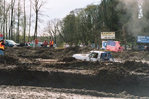 1990 Ford Bronco - A modified pickup truck navigates a challenging mud bog, with spectators watching the event.