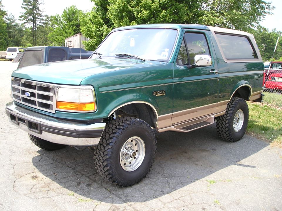 Green and tan lifted Ford Bronco SUV on mud tires, front 3/4 view in a lot