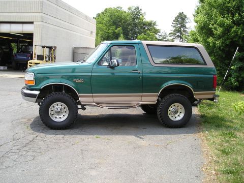 1996 Ford Bronco - Lifted green Ford Bronco with tan trim and chrome wheels parked on asphalt.