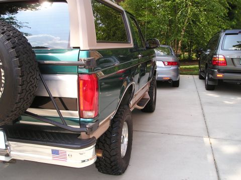 1996 Ford Bronco - A lifted green Ford Bronco is parked in a driveway, showing its rear end and spare tire.