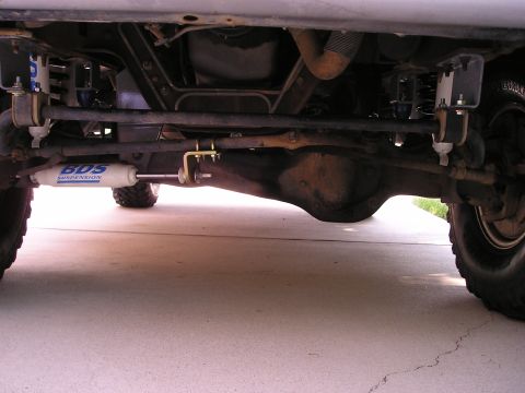 1996 Ford Bronco - The underside of a vehicle displays aftermarket suspension parts and a differential, indicating modifications for off-road use.