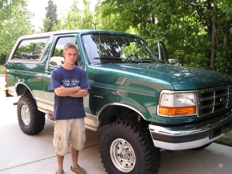 1996 Ford Bronco - A person stands beside a lifted green 1996 Ford Bronco with its driver's side door open.