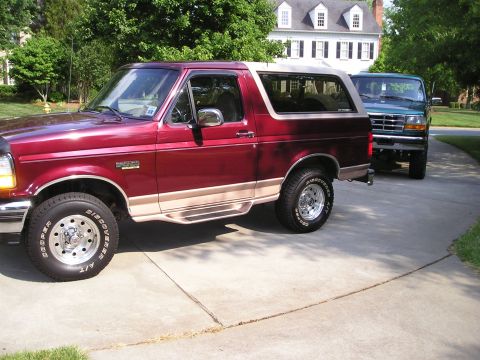 1996 Ford Bronco - Two Ford Broncos are parked on a driveway in front of a large house.