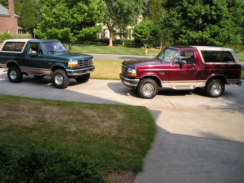 1996 Ford Bronco - Two Ford Broncos are parked on a suburban driveway on a sunny day.