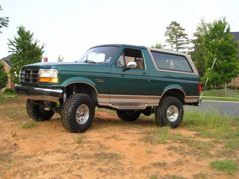 1996 Ford Bronco - A lifted 1996 Ford Bronco in green with tan accents sits on a dirt lot, ready for off-road adventure.