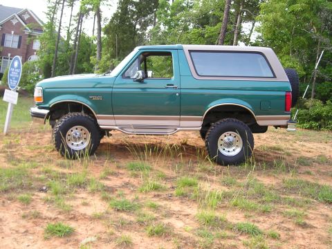 1996 Ford Bronco - This lifted 1996 Ford Bronco features a two-tone green and tan paint scheme and is parked outdoors on a dirt lot.