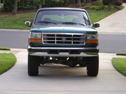 1996 Ford Bronco - This lifted green Ford truck is shown from the front, parked on a concrete driveway with grass on either side.