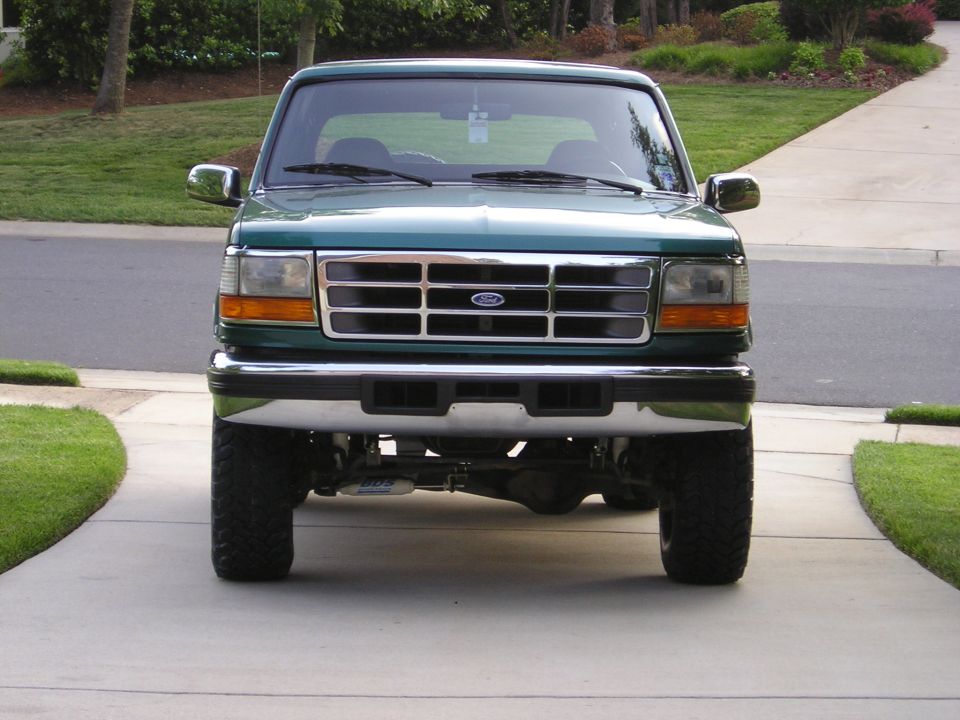 Lifted dark green Ford Bronco head-on in a driveway with chrome grille and oversized tires