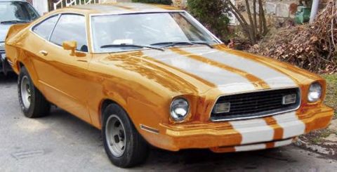 1974 Ford Mustang II - A 1974 Ford Mustang II coupe with distinctive orange and white racing stripes is parked on a street.