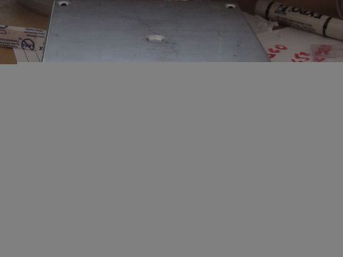 1987 Ford Bronco - A metal plate with pre-drilled holes sits on a surface next to some boxes and a marker.