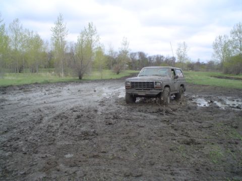 1981 Ford Bronco - A Ford Bronco navigates a challenging muddy terrain under an overcast sky.