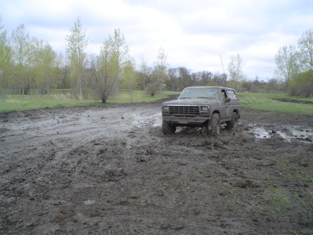 Mud-splattered gray Ford Bronco driving through a muddy field