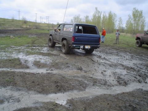 1981 Ford Bronco - A blue 1981 Ford Bronco navigates a muddy off-road course with another vehicle visible in the background.