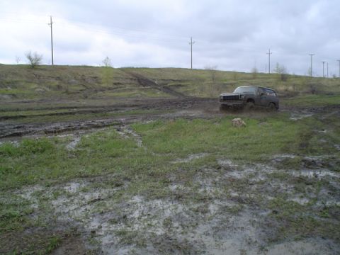 1981 Ford Bronco - Ford Bronco navigates a challenging muddy off-road course under an overcast sky.