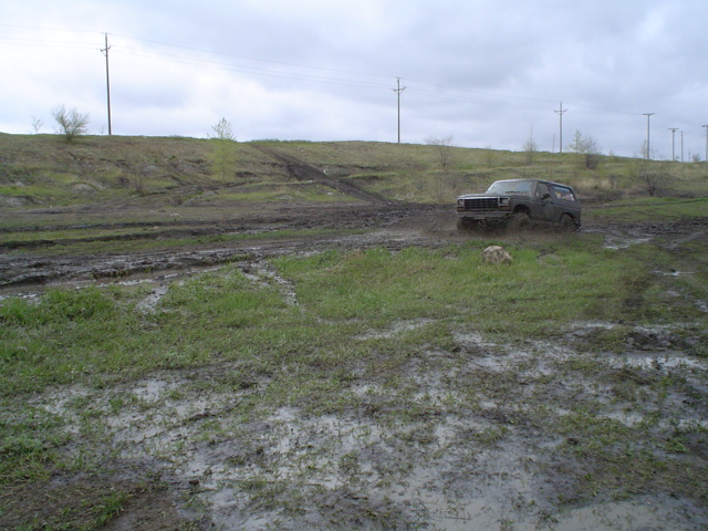 Dark colored 1980 Ford Bronco driving off-road through muddy terrain