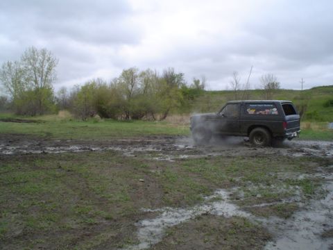 1981 Ford Bronco - A Ford Bronco navigates a muddy terrain under an overcast sky.