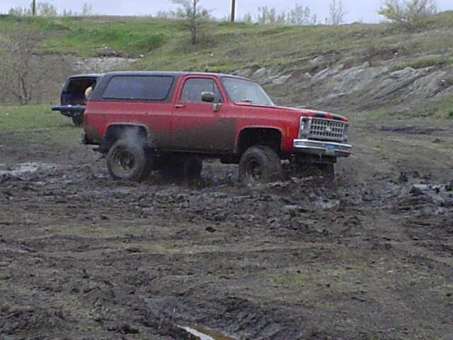Red lifted Chevy Blazer K5 on mud tires sitting in a muddy field, gray hood