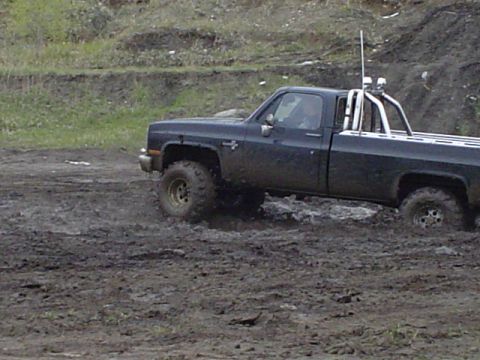 1981 Ford Bronco - A dark-colored pickup truck navigates a muddy terrain, kicking up water and dirt.
