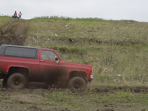 1981 Ford Bronco - Red SUV navigates a muddy terrain with a black hardtop.