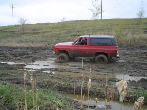 1981 Ford Bronco - Red Chevrolet K5 Blazer navigating a muddy off-road course.