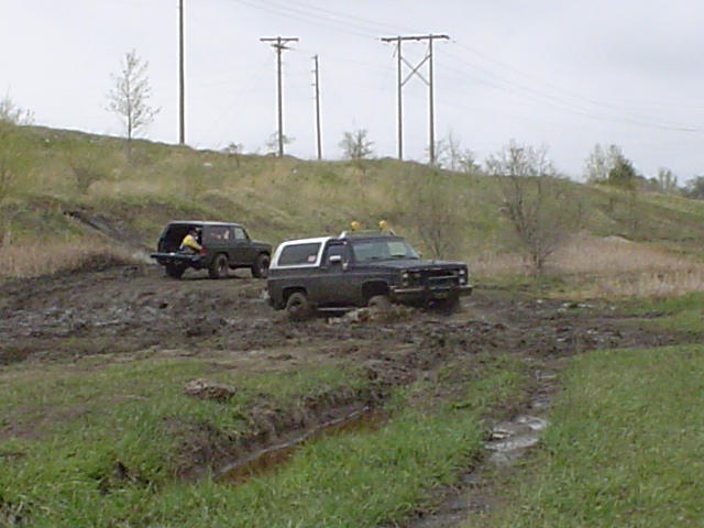 Two SUVs driving through a muddy field with power lines overhead