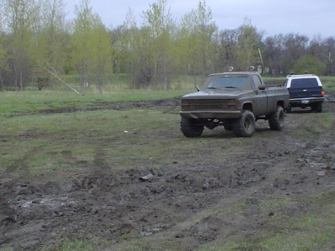 1981 Ford Bronco - Two off-road vehicles navigate a muddy terrain under an overcast sky.