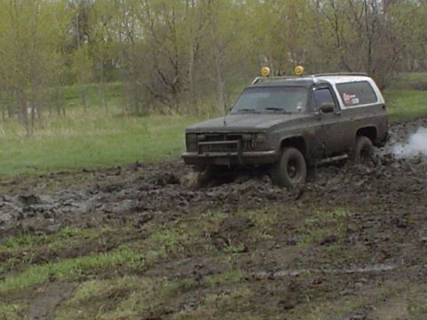 1981 Ford Bronco - This SUV is deep in the mud, struggling to move forward.