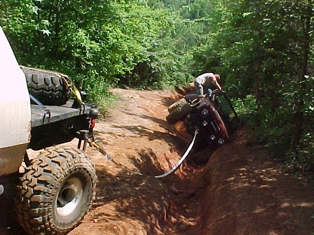 Truck winching a maroon SUV out of a ditch on a dirt trail