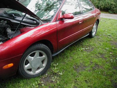 1997 Ford Taurus - The front passenger side of a red 1997 Ford Taurus is shown with the hood up, parked on a grassy area.