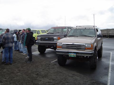1989 Ford Bronco - Two Ford SUVs, a tan Explorer and a black Bronco, are parked side-by-side with a group of people.