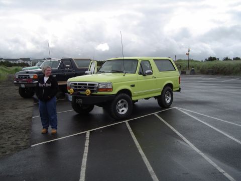 1989 Ford Bronco - A lime green Ford Bronco is parked on a wet asphalt lot with a woman standing nearby.